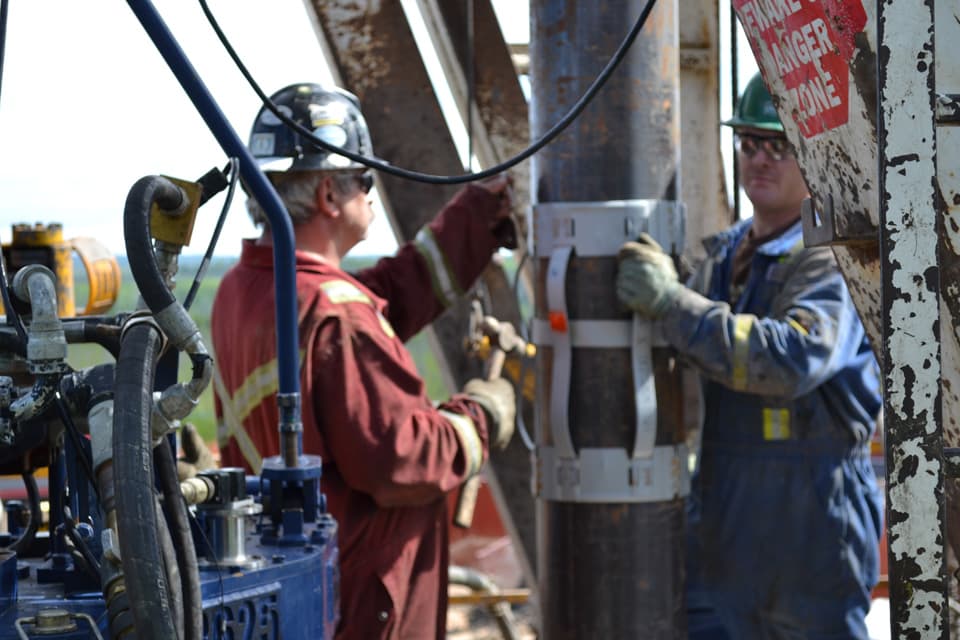Two Edcon operators in red coveralls guiding casing on the rig floor